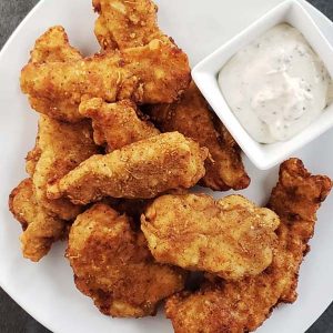 Close up of sourdough chicken strips on white plate.