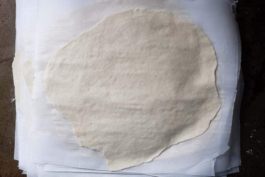 Stack of rolled out tortilla separated by parchment paper.