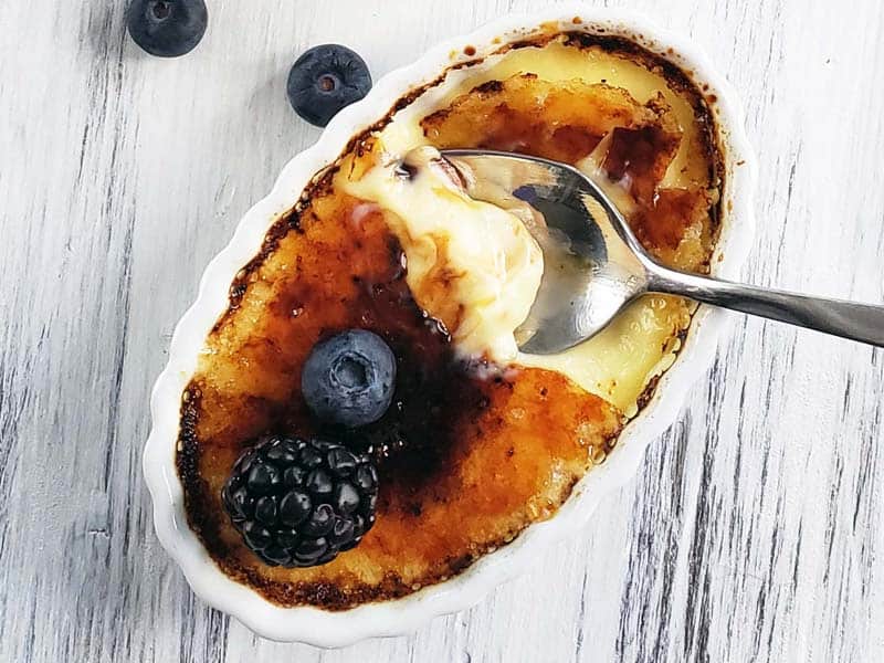 Spoon cracking the top of a creme brulee that is topped with fresh berries.