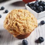 Mango blueberry muffin on a white surface surrounded by blueberries.