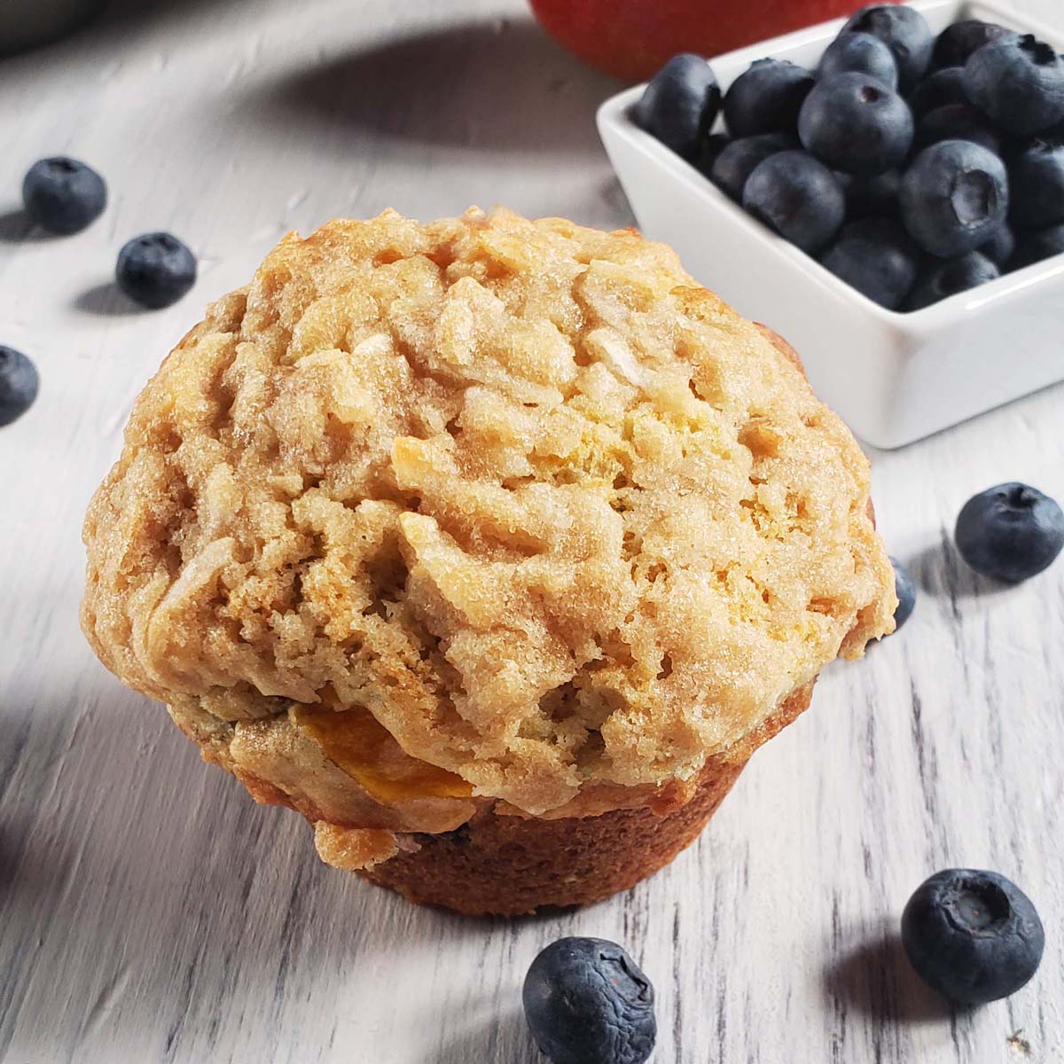 Mango blueberry muffin on a white surface surrounded by blueberries.