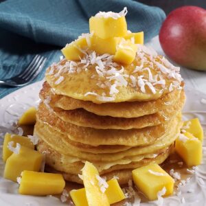 Close up of a stack of mango pancakes topped with cubed mango on a white plate.