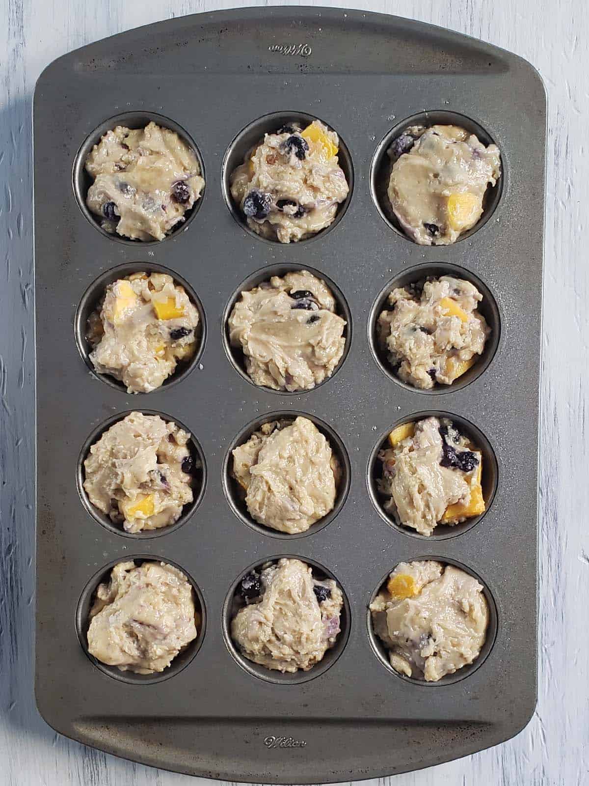 Mango blueberry muffin batter in muffin tin.