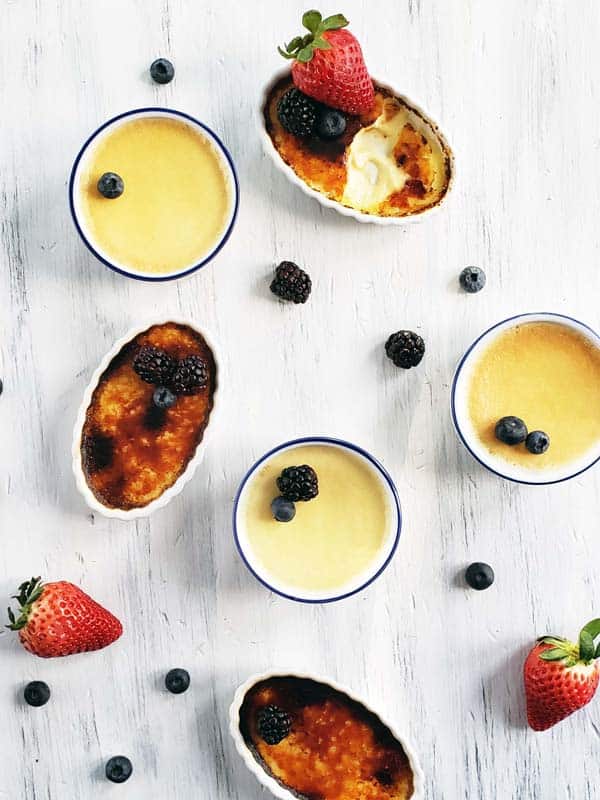 Six creme brulees topped with fruit on a white background.