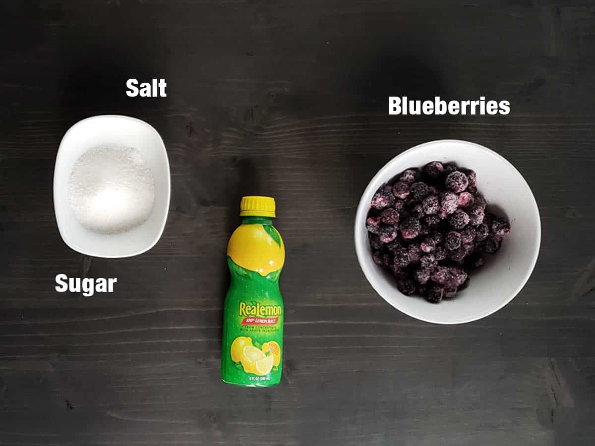 Blueberry jam ingredients on a dark surface.