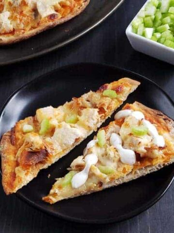 Two slices of buffalo chicken flatbread on a black plate.