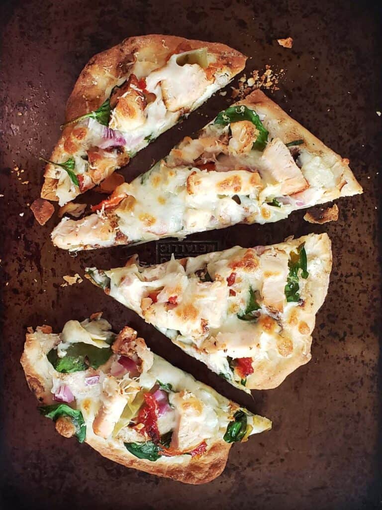 Slices of spinach chicken artichoke flatbread pizza on a baking sheet.