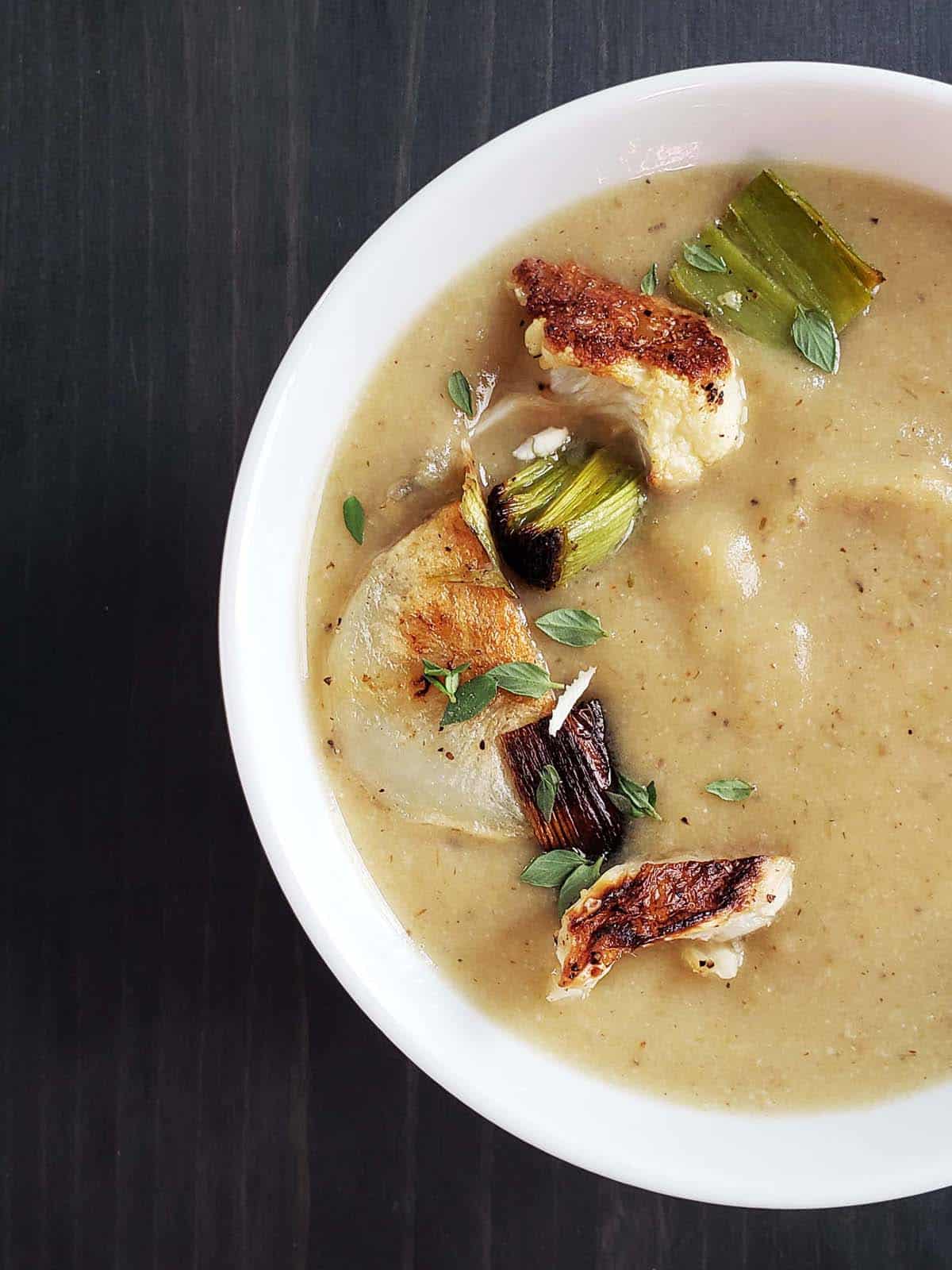 White bowl filled with roasted cauliflower leek and potato soup on a dark wood background.