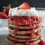 Stack or oatmeal strawberry pancakes topped with whipped cream and strawberries.