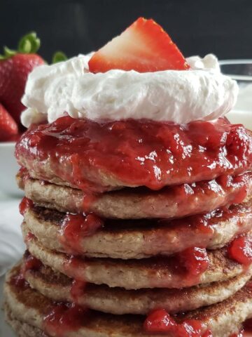 Stack or oatmeal strawberry pancakes topped with whipped cream and strawberries.