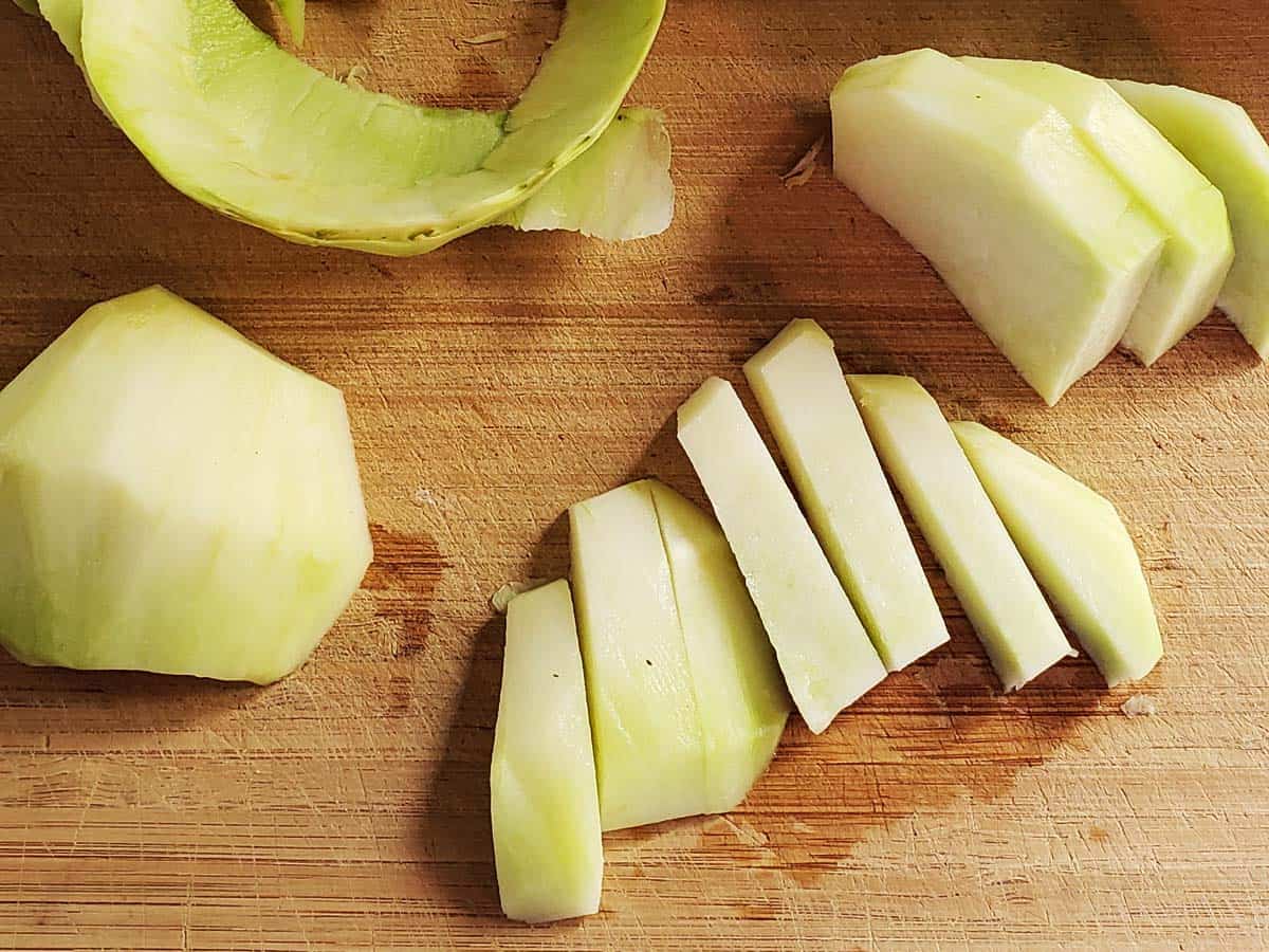 Kohlrabi sliced into even ½ inch sticks on a wooden cutting board.