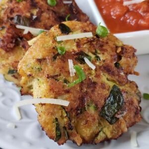 Close up of one chicken zucchini fritter on a white plate.