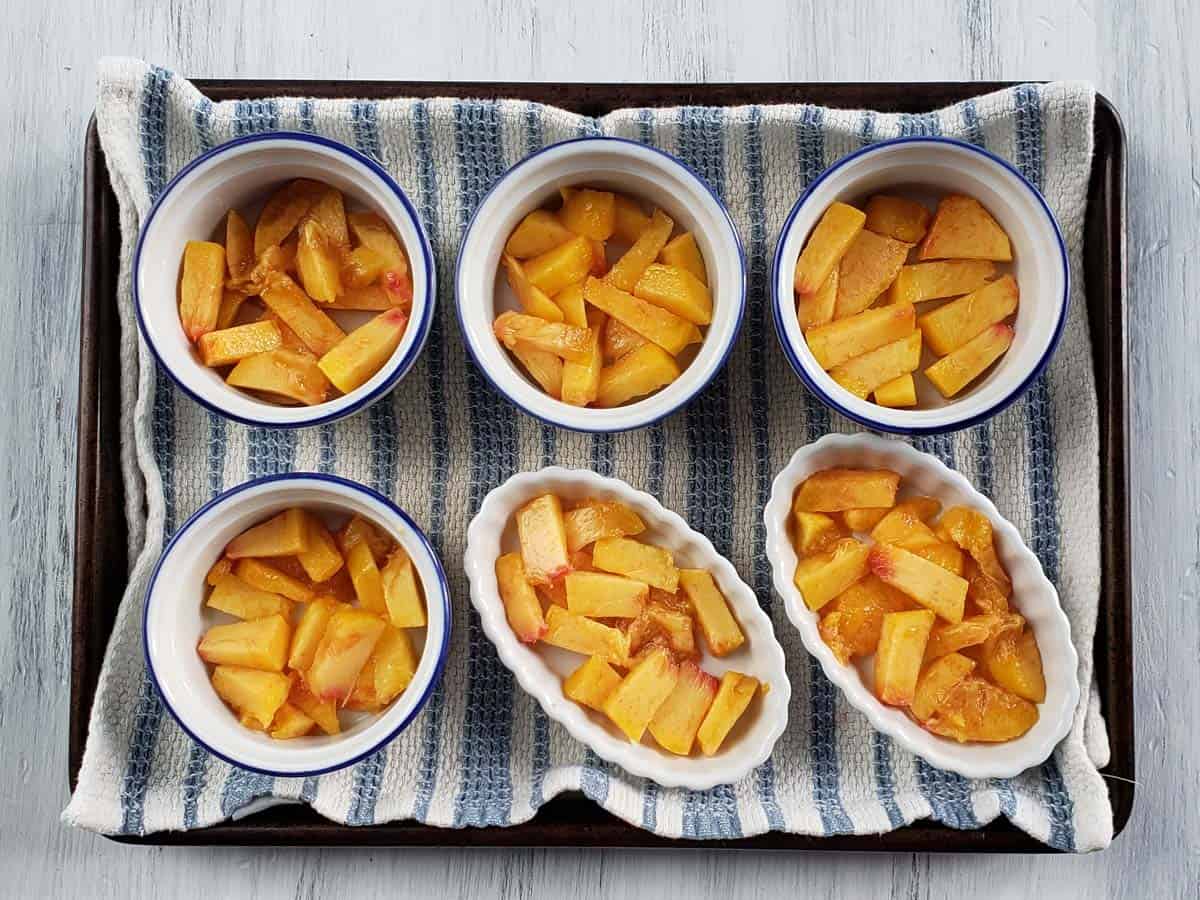 Ramekins on a baking sheet filled with chopped peaches.