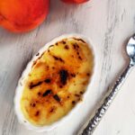 single peach creme brulee on a white wood surface