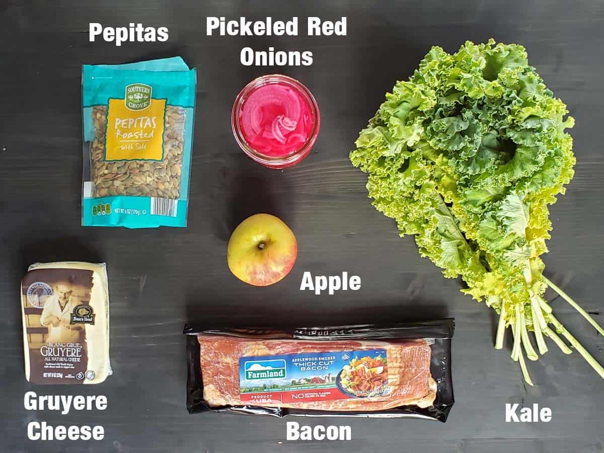 Kale apple salad ingredients on a dark surface.