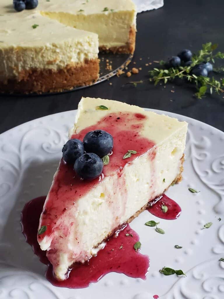 Slice of lemon thyme cheesecake topped with blueberry sauce and blueberries on a white plate.