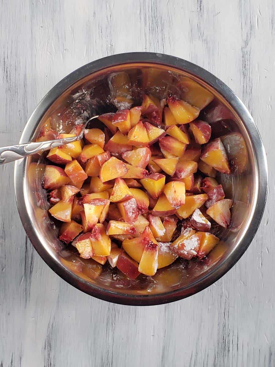 Diced peaches coated with cornstarch in a metal bowl.