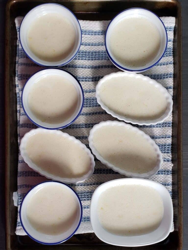 Ramekins filled with creme brulee in a towel lined baking sheet.
