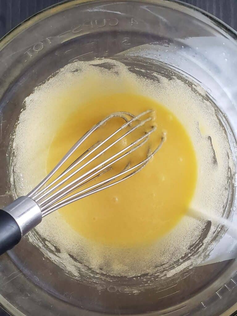 Whisked egg yolks and sugar in a glass measuring cup.
