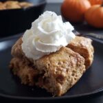 Close up of a slice of pumpkin cobbler topped with whipped cream.