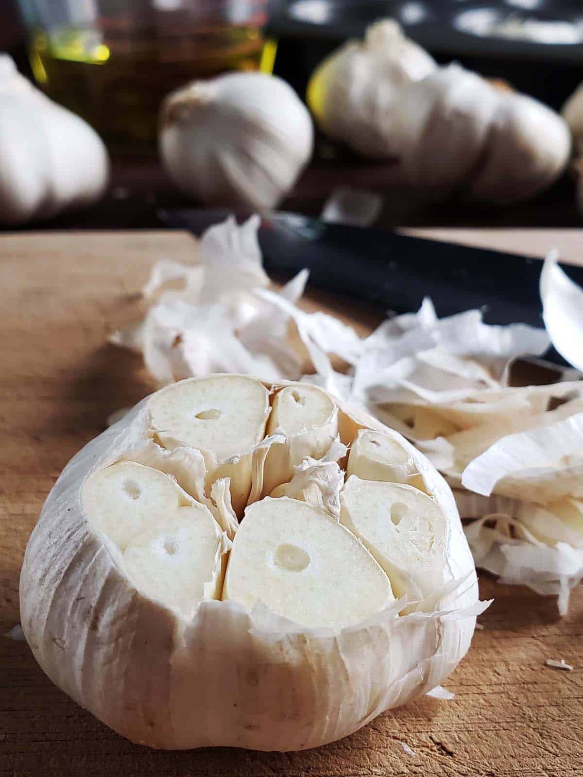 Head of garlic on top of a cutting board with the top sliced off.