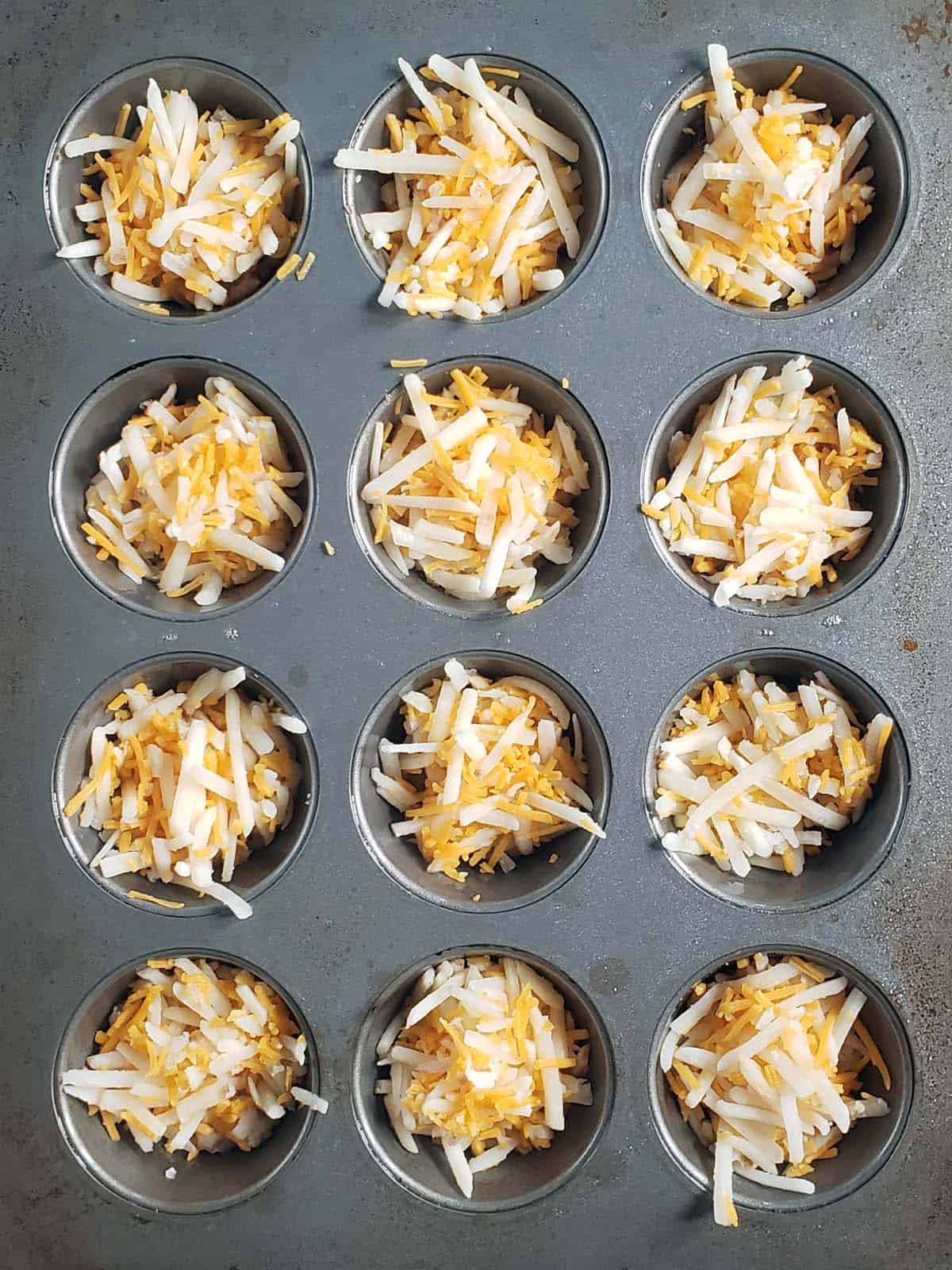 Hash browns and cheese in a muffin tin.