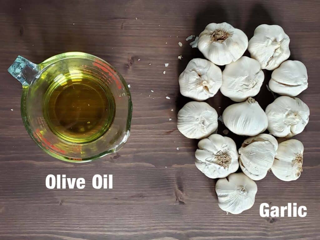 Olive oil and garlic heads on a wooden surface.
