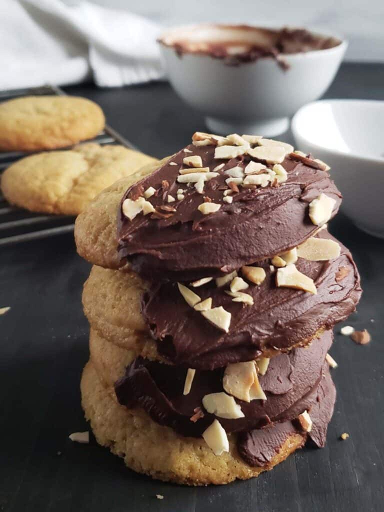 Stack of four amaretto sugar cookies on a dark surface.