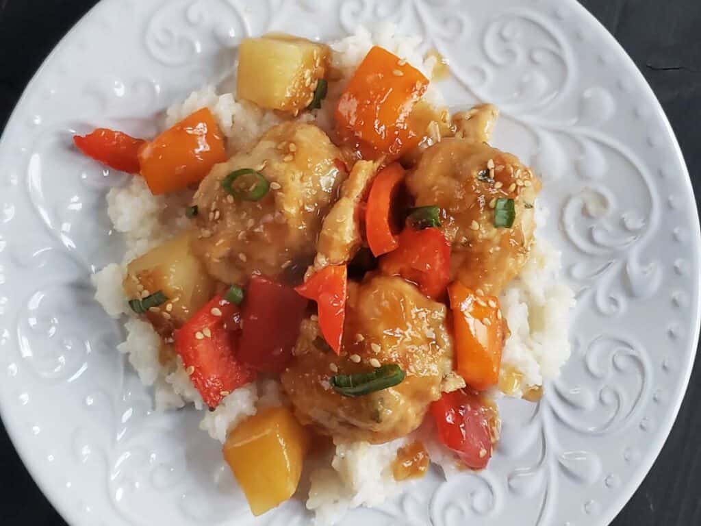 Chicken pineapple meatballs with pineapple, bell peppers, and rice on a white plate.