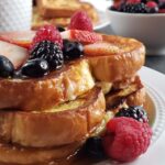 Stack of french toast topped with berries on a white plate