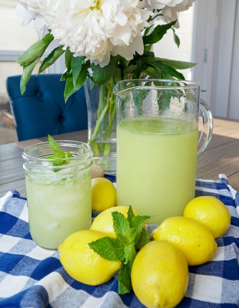 mint lemonade in a glass pitcher surrounded by lemons