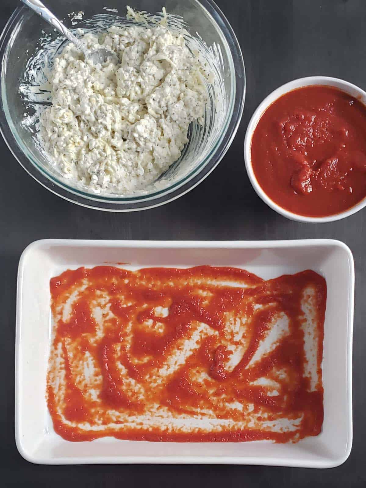 white casserole dish with a layer of spaghetti sauce