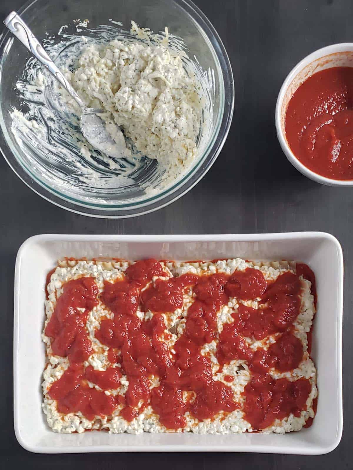 white casserole dish with dots of spaghetti sauce on top of cheese