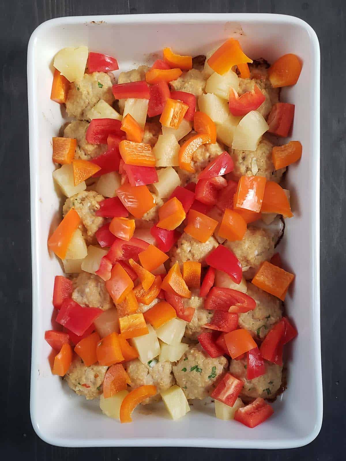 Chicken meatballs, bell peppers, and pineapple in a white casserole dish.