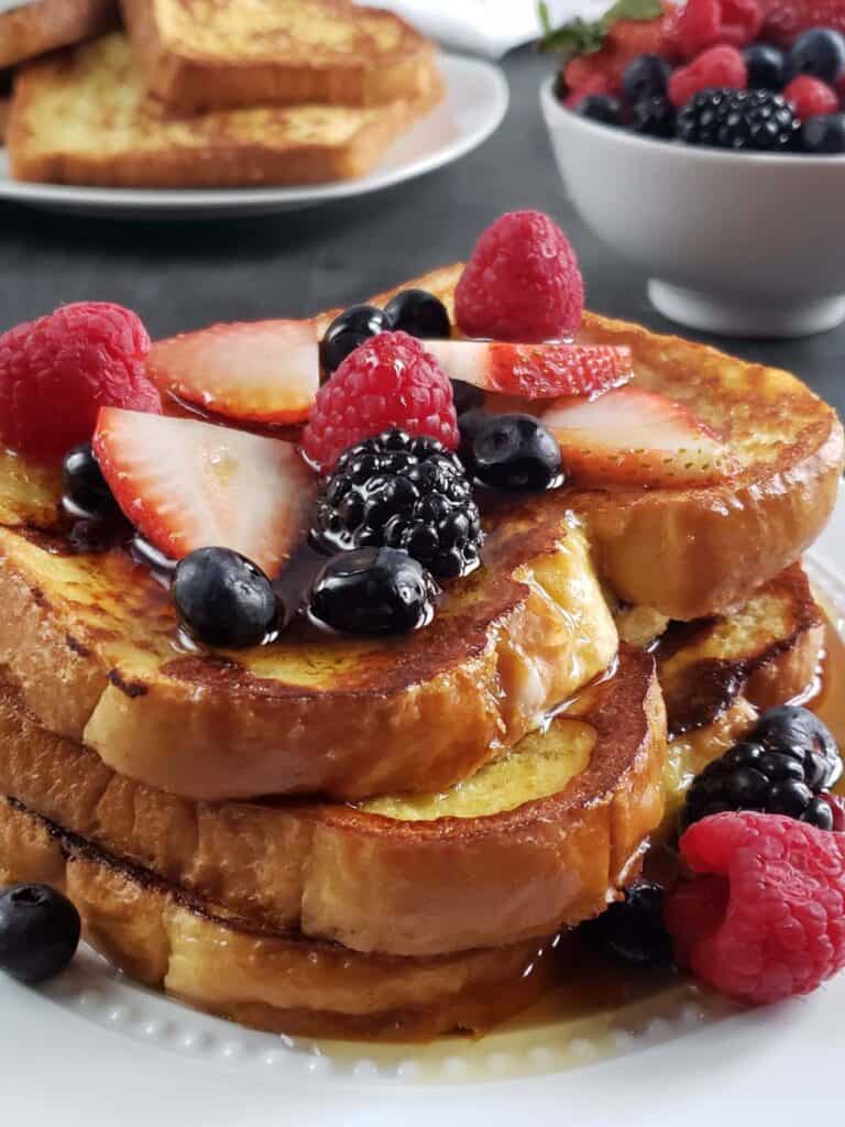 three slices of french toast topped with mixed berries on a white plate