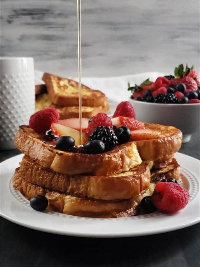 Stack of french toast topped with berries on a white plate