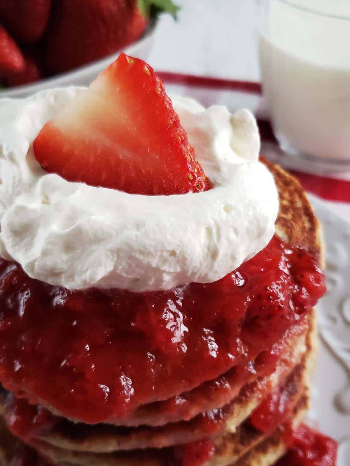 Stack or oatmeal strawberry pancakes topped with whipped cream and strawberries.