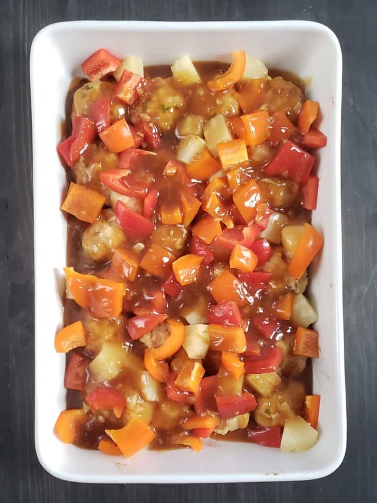 Meatballs, bell peppers, pineapple, and teriyaki sauce in a white casserole dish.