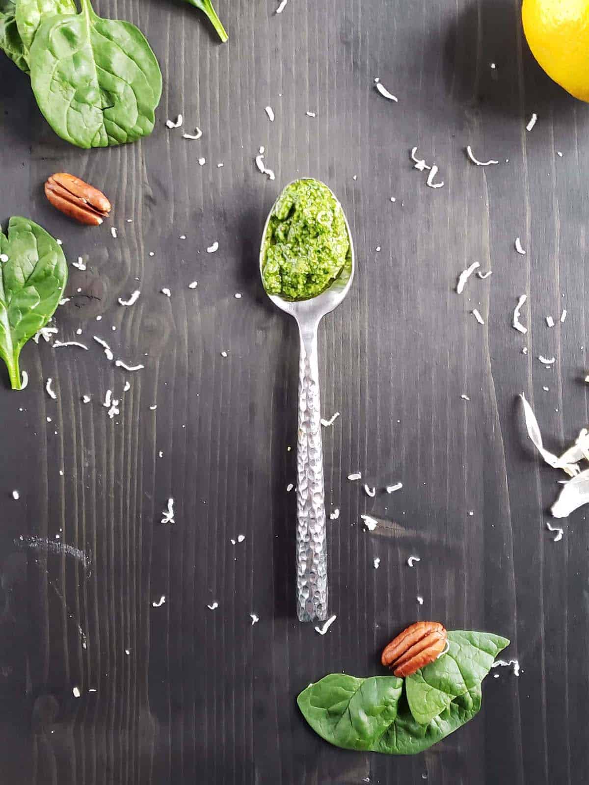 Spinach pesto on a metal spoon resting on a dark wood surface.
