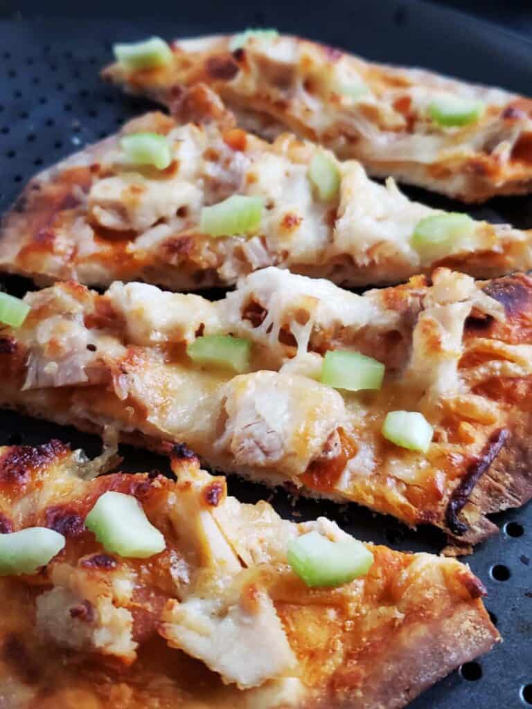 Slices of buffalo chicken flatbread pizza on a pizza pan.