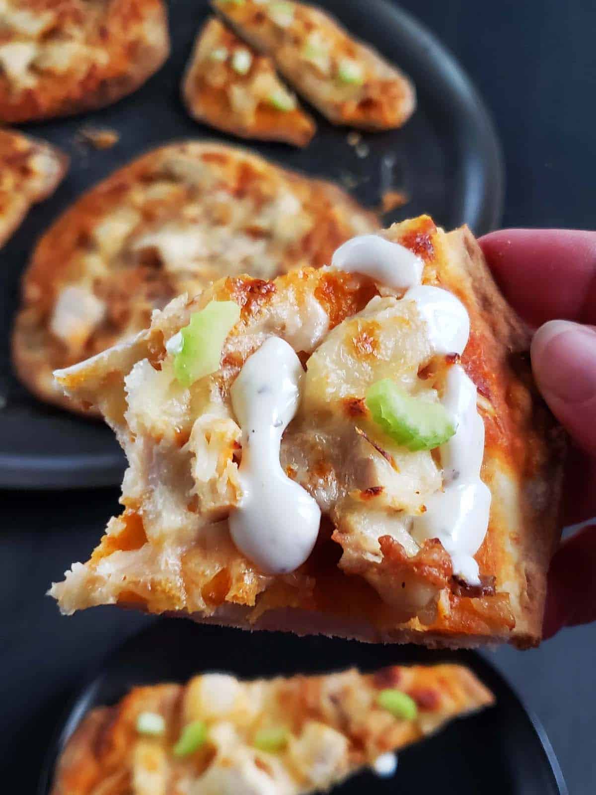 Close up of a slice of buffalo chicken flatbread pizza with a bite missing.