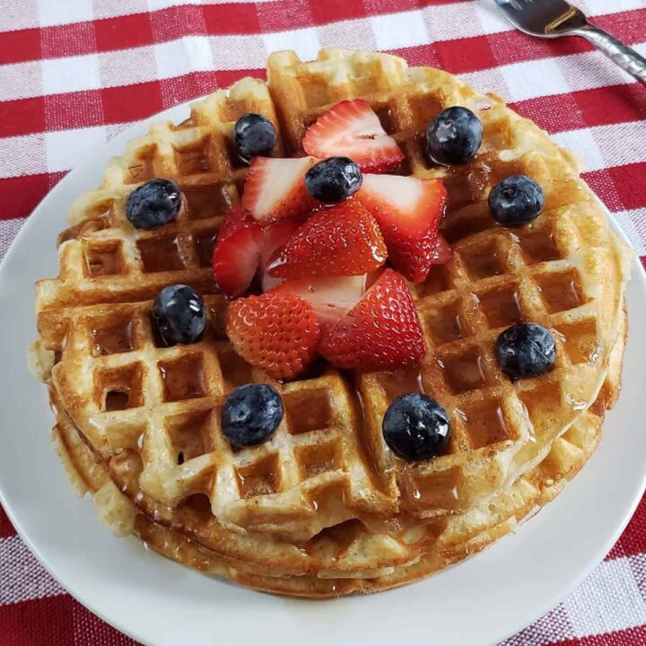 Stack of waffles topped with berries on a white plate.