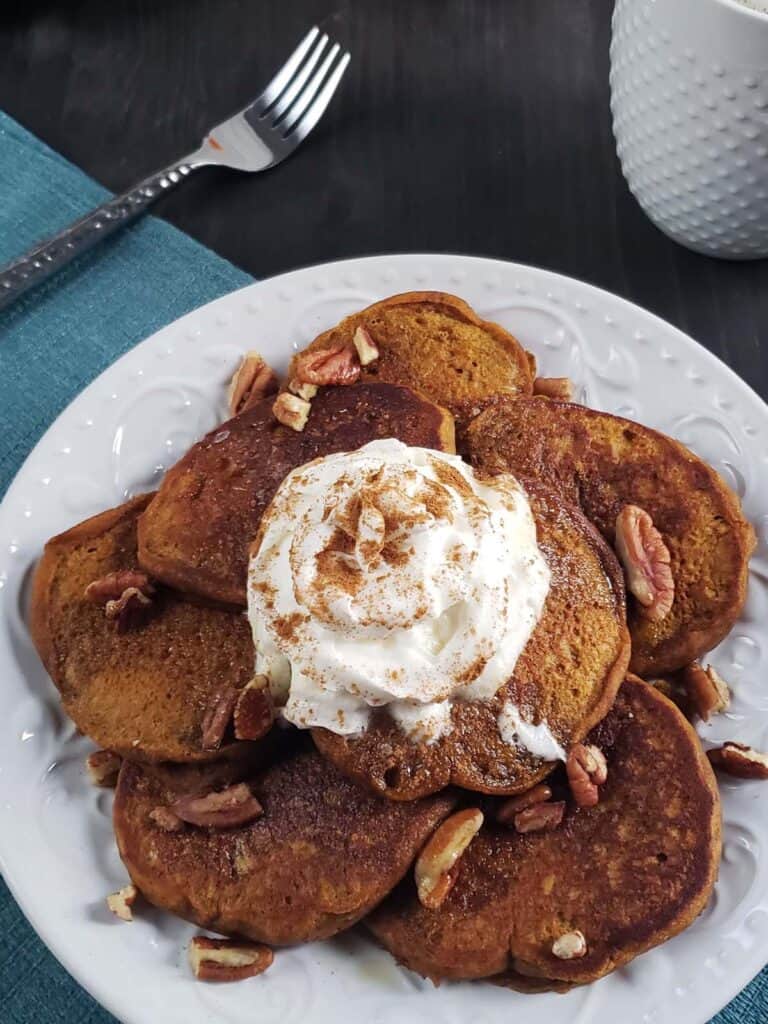 Stack of pumpkin spice latte pancakes on a white plate topped with whipped cream.