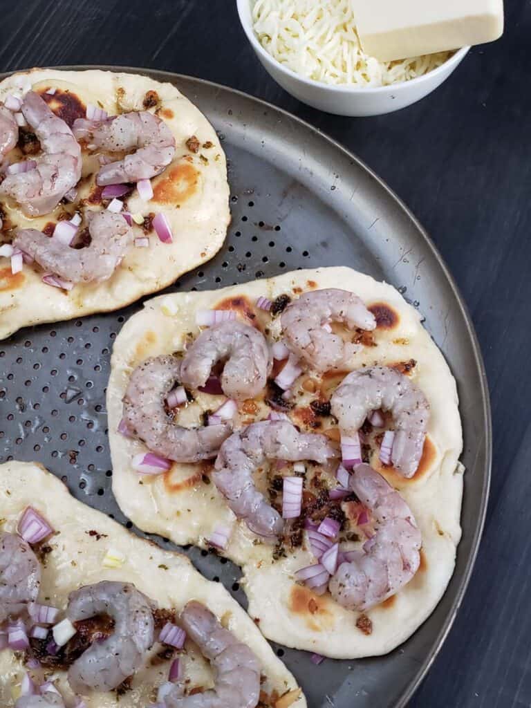 Three uncooked shrimp scampi flatbread pizzas without cheese on a pizza pan.