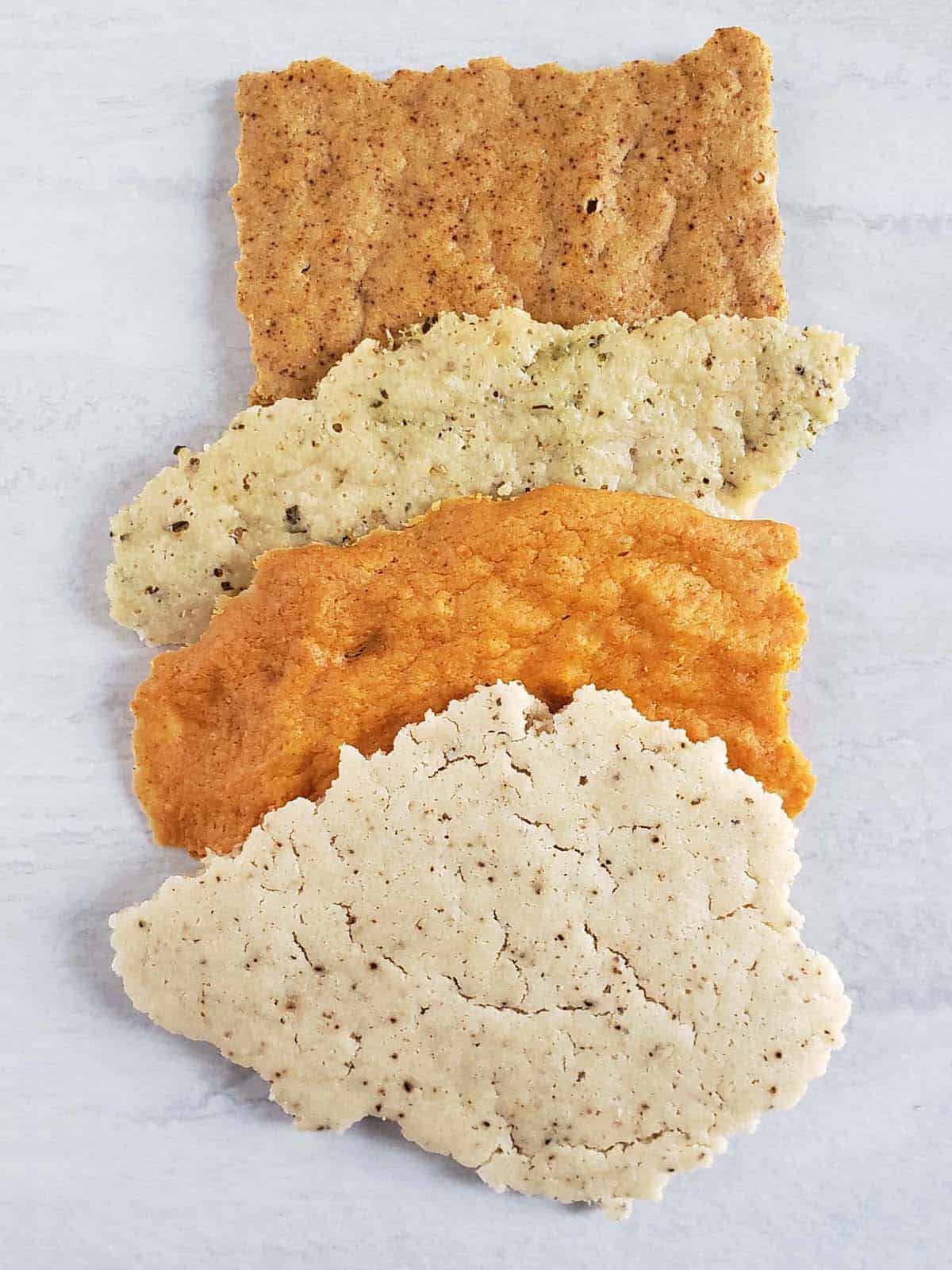 Four different flavors of sourdough crackers on a white surface.
