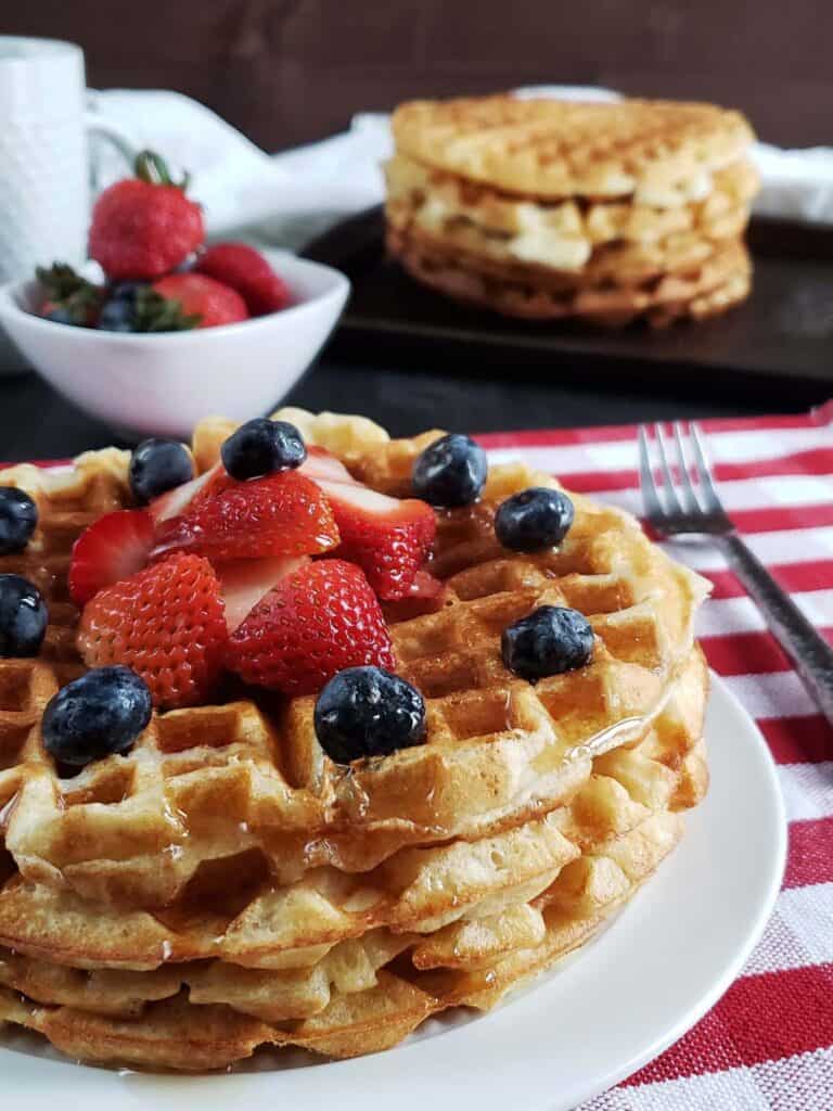 Stack of waffles topped with berries on a white plate.