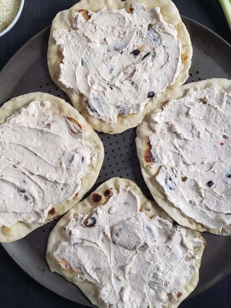 Flatbread spread with cream cheese on a pizza pan.