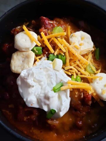 Close-up of a bowl of chili topped with sour cream, cheese, and oyster crackers.