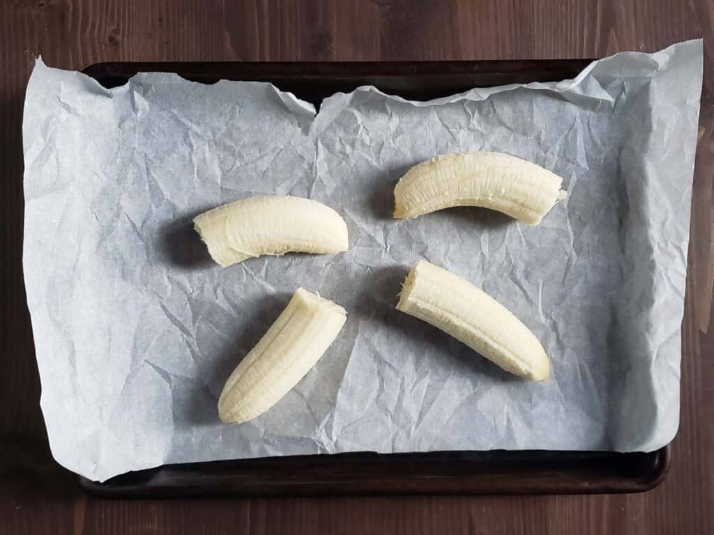 Frozen bananas on a parchment paper lined baking sheet.