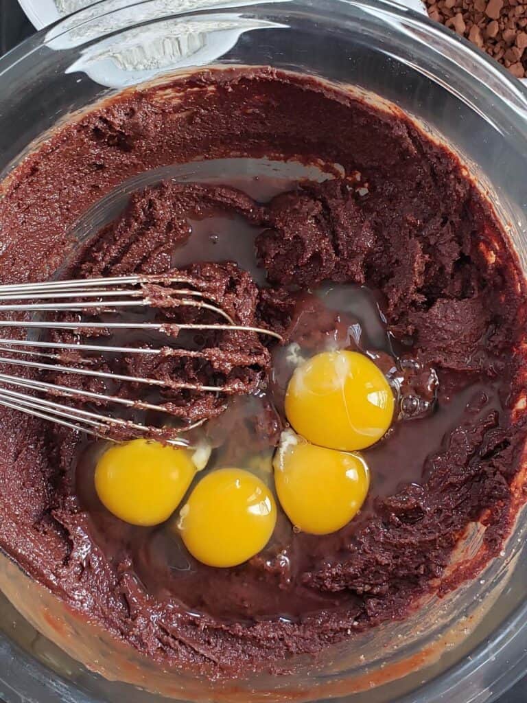 Brownie batter topped with eggs in a glass bowl.